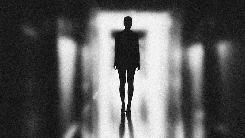 Black and white silhouette of a teenager standing in a passage with strong backlighting